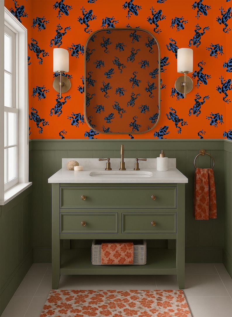 May include: A bathroom with orange walls patterned with blue frog illustrations. The vanity is olive green with a white countertop and gold fixtures. A matching rug and towel complete the design.