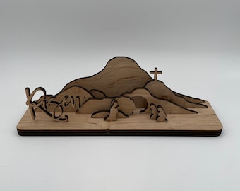 May include: Wooden Easter scene with a mountain, a cross, and the word "risen" carved into the base. Two figures are carved into the scene, one kneeling and one standing.