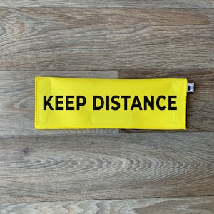 May include: Yellow fabric floor sign with the text "KEEP DISTANCE" in black lettering.