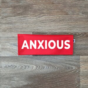 May include: A red fabric pouch with the word "ANXIOUS" printed in white letters.