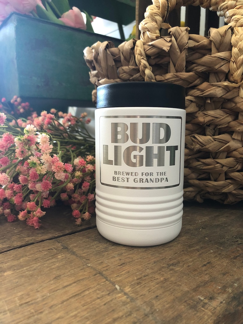 May include: White insulated beverage holder with a black lid. The holder has a silver sticker with the text "Bud Light" and "Brewed for the Best Grandpa".