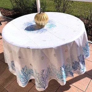 May include: A round white tablecloth with a blue and teal coral reef design. A gold-colored decorative glass pumpkin sits on the table. The tablecloth has a scalloped edge.