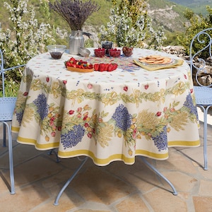 May include: A round table with a white tablecloth featuring a floral pattern, set with a bowl of fruit, a pitcher, and a plate of pastries. Two blue metal chairs are placed on either side of the table, overlooking a scenic mountain view.