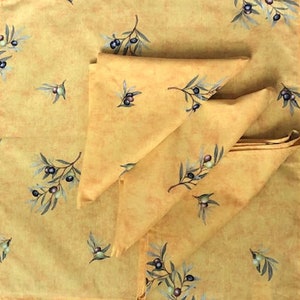 May include: Three yellow fabric napkins with a repeating olive branch pattern. The napkins are folded and stacked on top of each other.