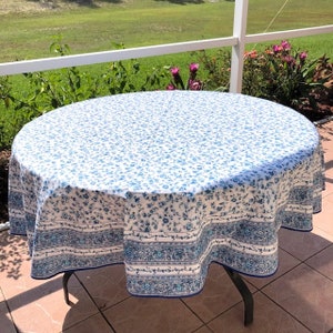 May include: A round tablecloth with a white background and a blue floral pattern. The border features a blue and white floral design. The tablecloth is draped over a dark metal table.