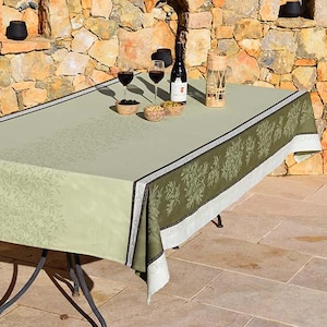 Puede incluir: Un mantel de mesa verde y blanco con un patrón floral. El mantel está puesto sobre una mesa con dos copas de vino y una botella de vino.