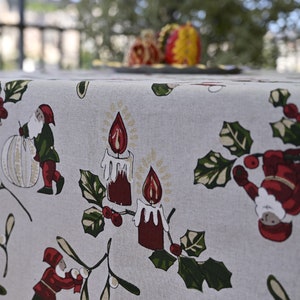 May include: A white tablecloth with a festive Christmas design featuring red candles, holly leaves, and green gnomes. The tablecloth has a subtle linen texture.