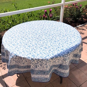 May include: A round tablecloth with a white background and a pattern of small blue flowers. The border features a decorative blue and white design. The tablecloth is on a round table.