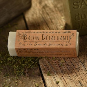 May include: A rectangular, light-colored soap bar with a brown paper label. The label reads "BATON DÉTACHANT" and "à la Terre de Sommières" in elegant script. The bar rests on a rustic wooden surface.