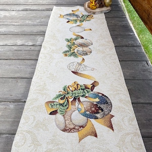 May include: A white table runner with a gold and green Christmas ornament design. The ornaments are strung together with gold ribbon and bows.