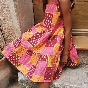 May include: A sleeveless, tiered dress with a patchwork design in shades of pink, orange, and brown. The dress has a square neckline and a ruffled hem.