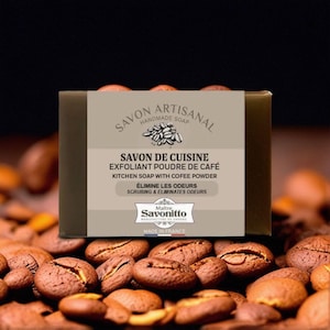 May include: A rectangular bar of handmade kitchen soap with coffee powder, labeled "Savon Artisanal." The soap is brown with a light brown label featuring text in French and English. The soap is surrounded by coffee beans.
