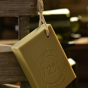 May include: A bar of olive oil soap with a brown rope attached. The soap has a circular stamp that reads "72% Savon de Marseille".