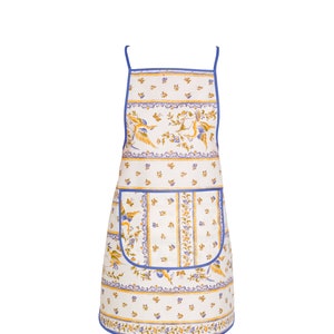 Puede incluir: Un delantal blanco con ribete azul y un estampado floral con pájaros y flores. El delantal tiene un bolsillo grande en la parte delantera.