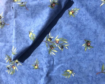 May include: A blue tablecloth with a pattern of olive branches and olives. The tablecloth is folded in half and has a napkin on top of it.