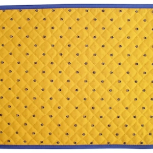May include: A yellow quilted placemat with a blue border and a small, repeating pattern of black flowers.