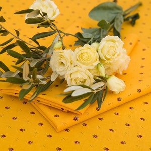 Puede incluir: Un ramo de rosas blancas con hojas verdes sobre un mantel amarillo con un patrón floral rojo.