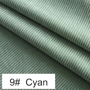 May include: A light sage green corduroy fabric featuring a distinct vertical ribbed texture with soft folds. A white rectangular label in the bottom left corner displays the black text 9# Cyan, indicating the color variant of this textile material.