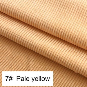 May include: A pale yellow corduroy fabric featuring a distinct vertical ribbed texture. The material is folded to show multiple layers of the soft, ridged surface. A white rectangular label in the corner displays the text 7# Pale yellow.