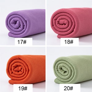 May include: Four rolls of ribbed fabric in various colors: purple, pink, orange, and green. Each roll is labeled with a number. The fabric appears to be tightly rolled, showcasing the texture and color variations. Ideal for crafting or sewing projects.