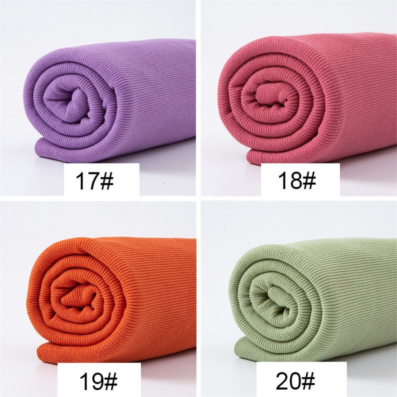 May include: Four rolls of ribbed fabric in various colors: purple, pink, orange, and green. Each roll is labeled with a number. The fabric appears to be tightly rolled, showcasing the texture and color variations. Ideal for crafting or sewing projects.