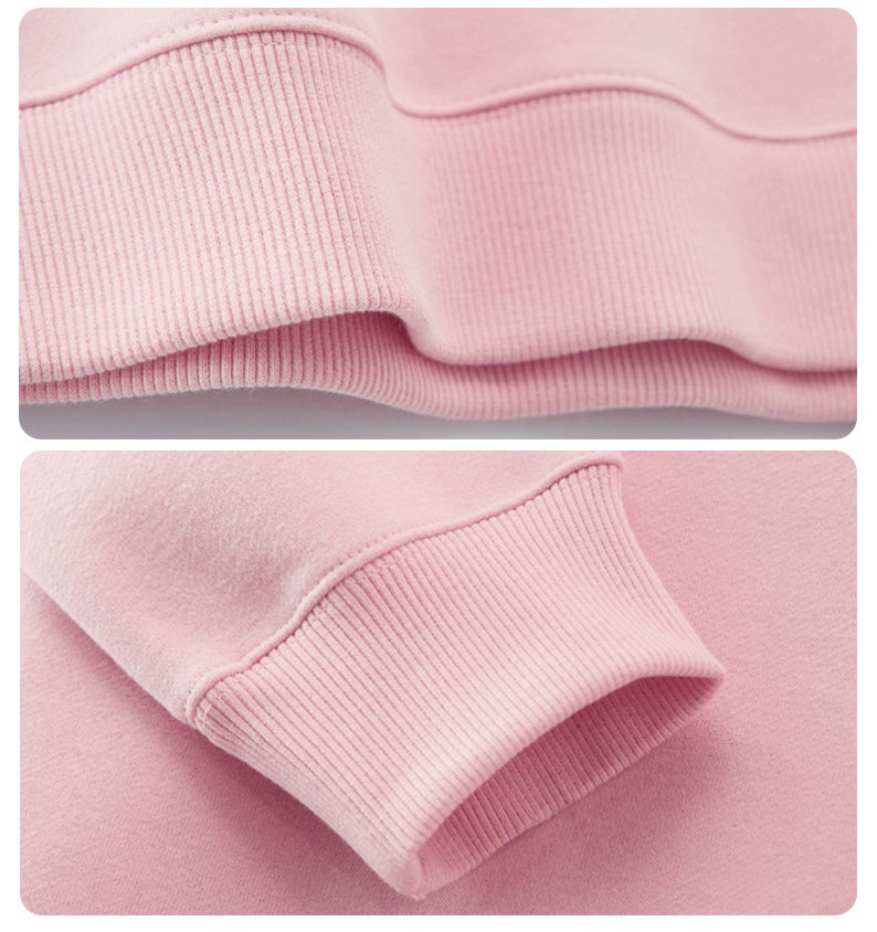 May include: Close-up of a light pink sweatshirt. The image highlights the ribbed cuffs and hem of the garment, showcasing the texture and stitching details. The fabric appears soft and comfortable, suggesting a casual style.