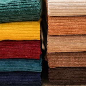May include: A stack of corduroy fabric swatches in various colors, including teal, yellow, red, blue, brown, and beige. The fabric has a ribbed texture.
