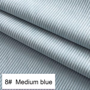 May include: A light blue corduroy fabric featuring a distinct vertical ribbed texture. The material is folded into three layers, showcasing the consistent weave and soft appearance of the textile. A white label displays the text 8# Medium blue.