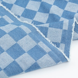 May include: Blue and white checkered fabric with a frayed edge. The fabric has a denim texture.