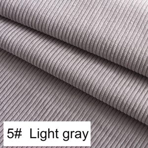 May include: A light gray corduroy fabric featuring a distinct vertical ribbed texture. The material is folded into multiple layers, showcasing the consistent parallel lines of the weave. A white rectangular label displays the text 5# Light gray.