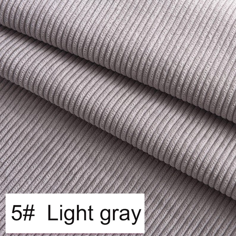 May include: A light gray corduroy fabric featuring a distinct vertical ribbed texture. The material is folded into multiple layers, showcasing the consistent parallel lines of the weave. A white rectangular label displays the text 5# Light gray.