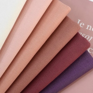 May include: A collection of seven fabric swatches in various shades of pink, red, and purple. The swatches are arranged in a fan shape, with the lightest shade at the top and the darkest shade at the bottom.