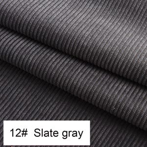 May include: A slate gray corduroy fabric featuring a distinct vertical ribbed texture. The material is folded into multiple layers, showcasing the consistent parallel lines of the weave. A white label at the bottom displays the text 12# Slate gray.