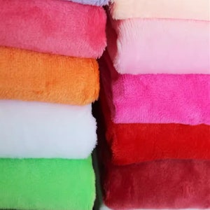May include: A stack of plush fabric in various colours, including purple, pink, orange, white, green, red, and burgundy. The fabric is soft and fuzzy, and it would be perfect for making blankets, cushions, or other crafts.