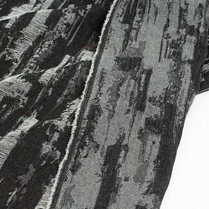 May include: Black and white fabric with a textured, abstract pattern. The fabric has a frayed edge.