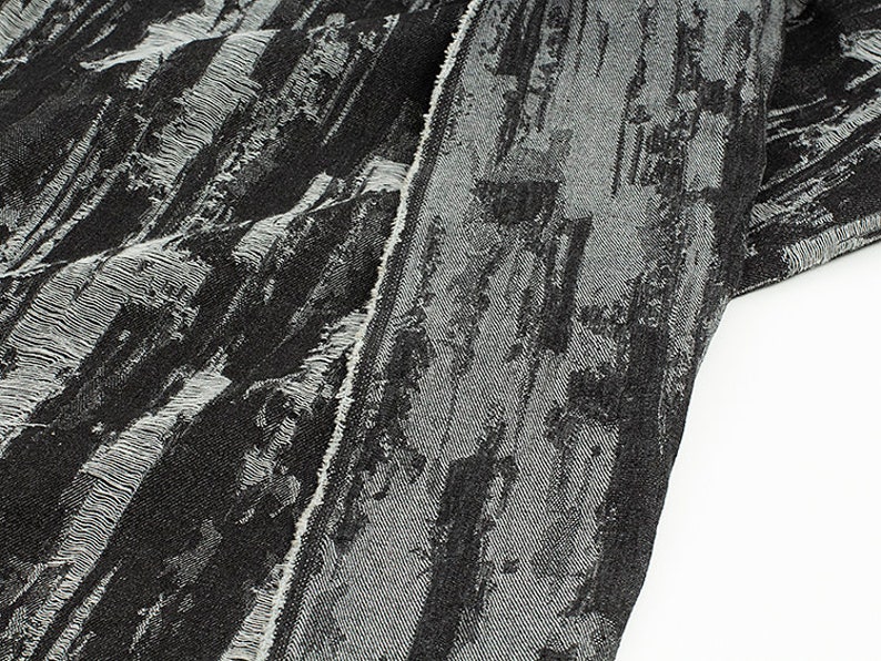 May include: Black and white fabric with a textured, abstract pattern. The fabric has a frayed edge.
