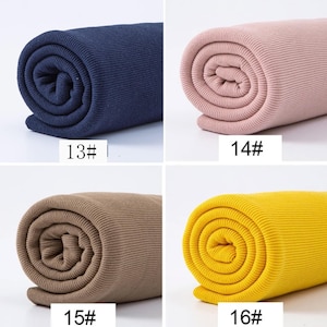 May include: Four rolls of ribbed fabric in navy blue, pink, tan, and yellow. Each roll is tightly wound, displaying the fabric's texture. The numbers 13#, 14#, 15#, and 16# are printed on the fabric.