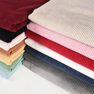 May include: A stack of folded ribbed fabric pieces in various colors including burgundy, black, light pink, red, white, navy blue, dark gray, light gray, sage green, yellow, tan, and light blue, all featuring a consistent vertical texture.