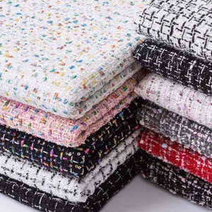 May include: A stack of colorful tweed fabric swatches in various patterns and colors, including white, black, pink, red, and gray.