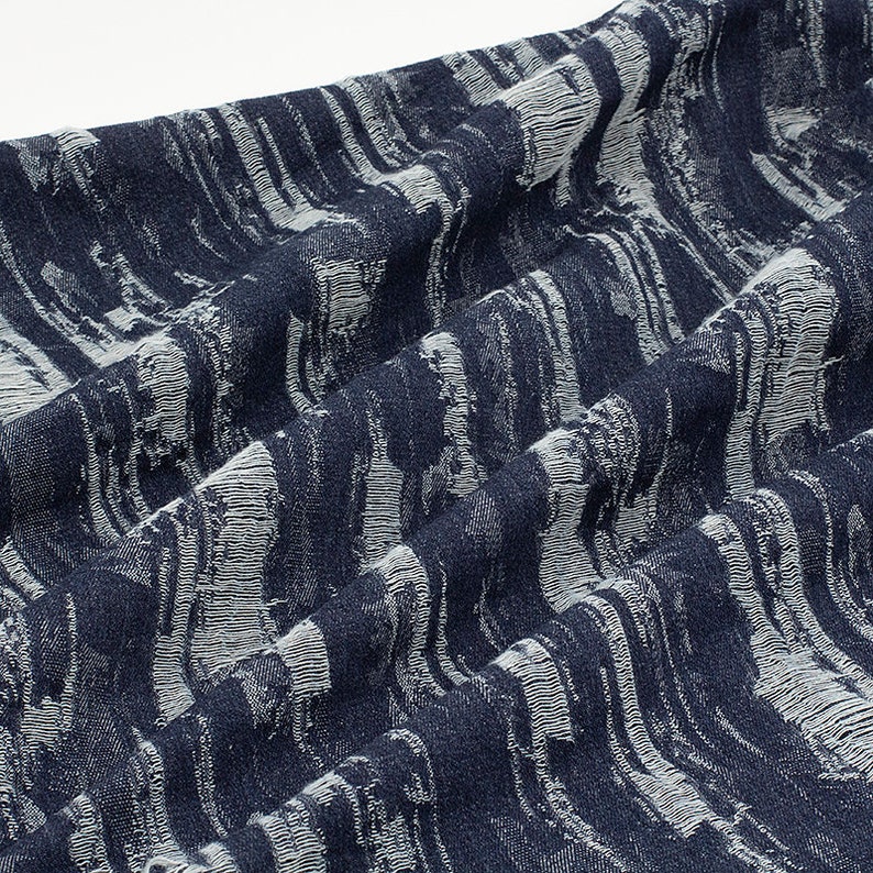 May include: Close-up of a blue fabric with a white textured pattern. The fabric has a woven look and feel.