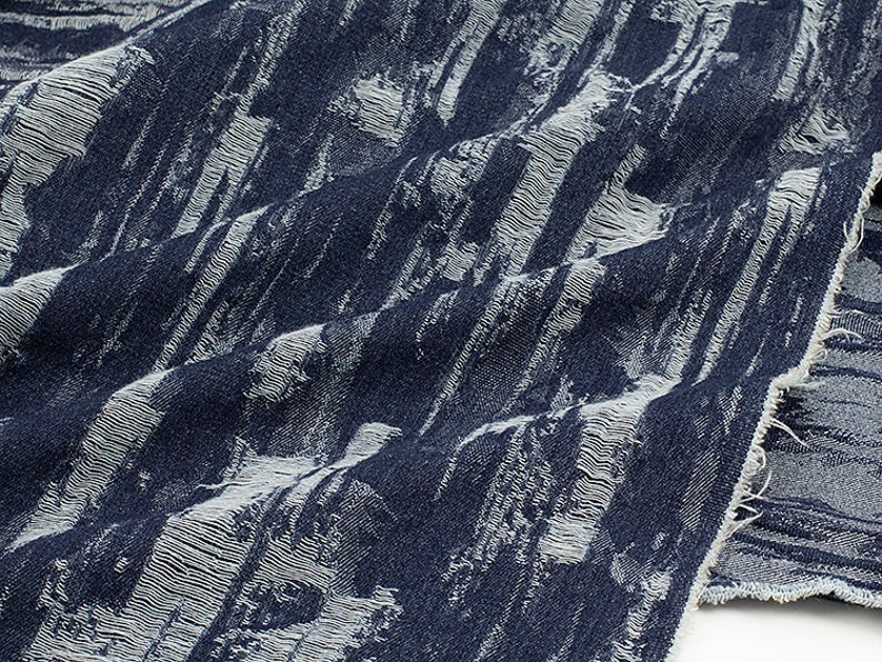 May include: Close-up of a blue and white textured fabric with a frayed edge. The fabric has a vertical striped pattern.
