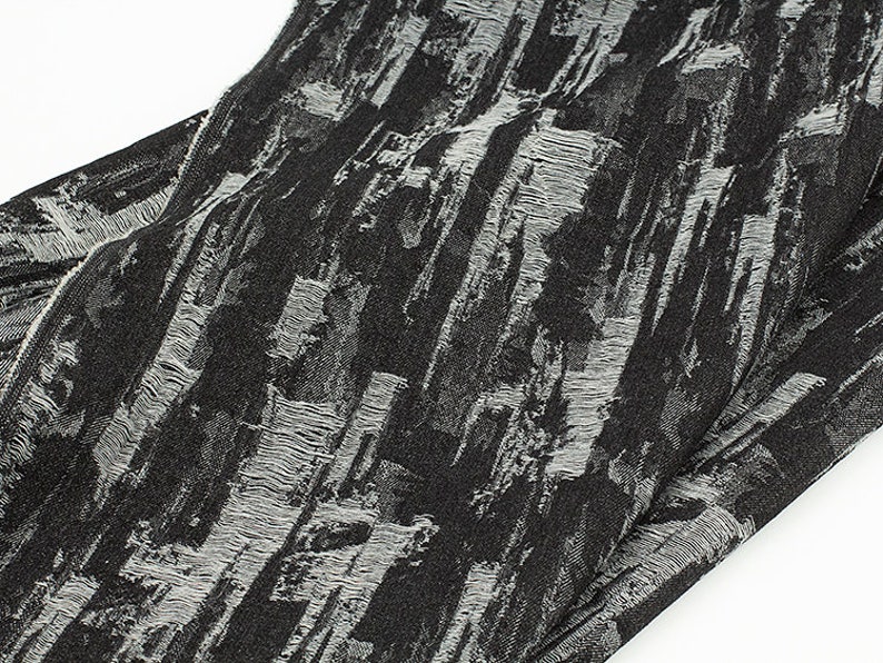 May include: Black fabric with a white textured pattern. The fabric has a slightly frayed edge.
