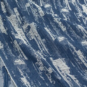May include: Close-up of blue denim fabric with a white distressed pattern. The fabric has a textured, worn look.