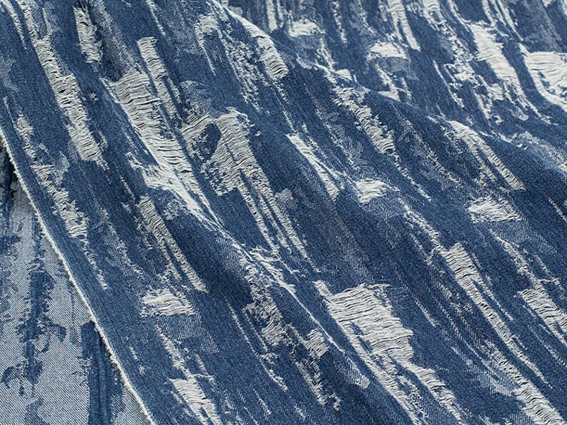 May include: Close-up of blue denim fabric with a white distressed pattern. The fabric has a textured, worn look.