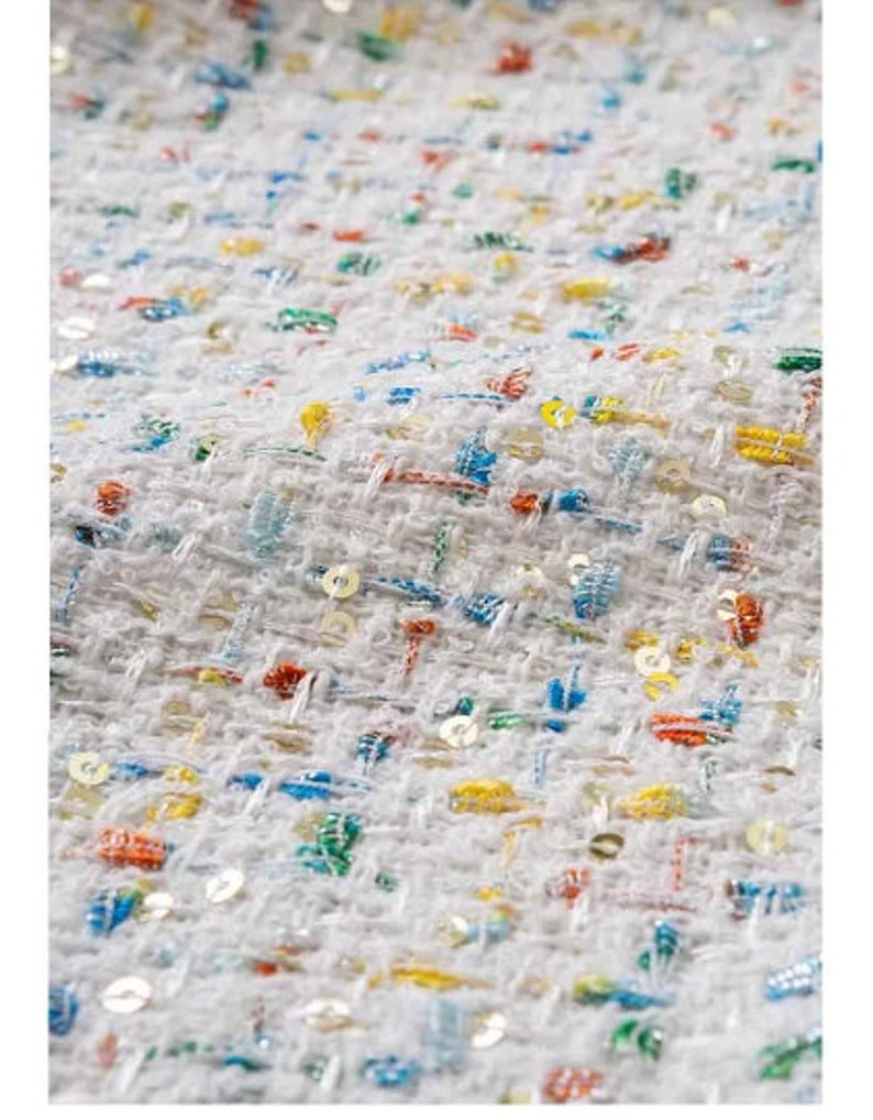 May include: White fabric with a woven texture and colorful sequins. The fabric has a subtle pattern of small squares.