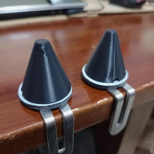 Può includere: Due oggetti neri a forma di cono con base ad anello bianca e clip metalliche. Gli oggetti sono su una superficie di legno. Le clip sono argentate e sembrano essere di metallo.