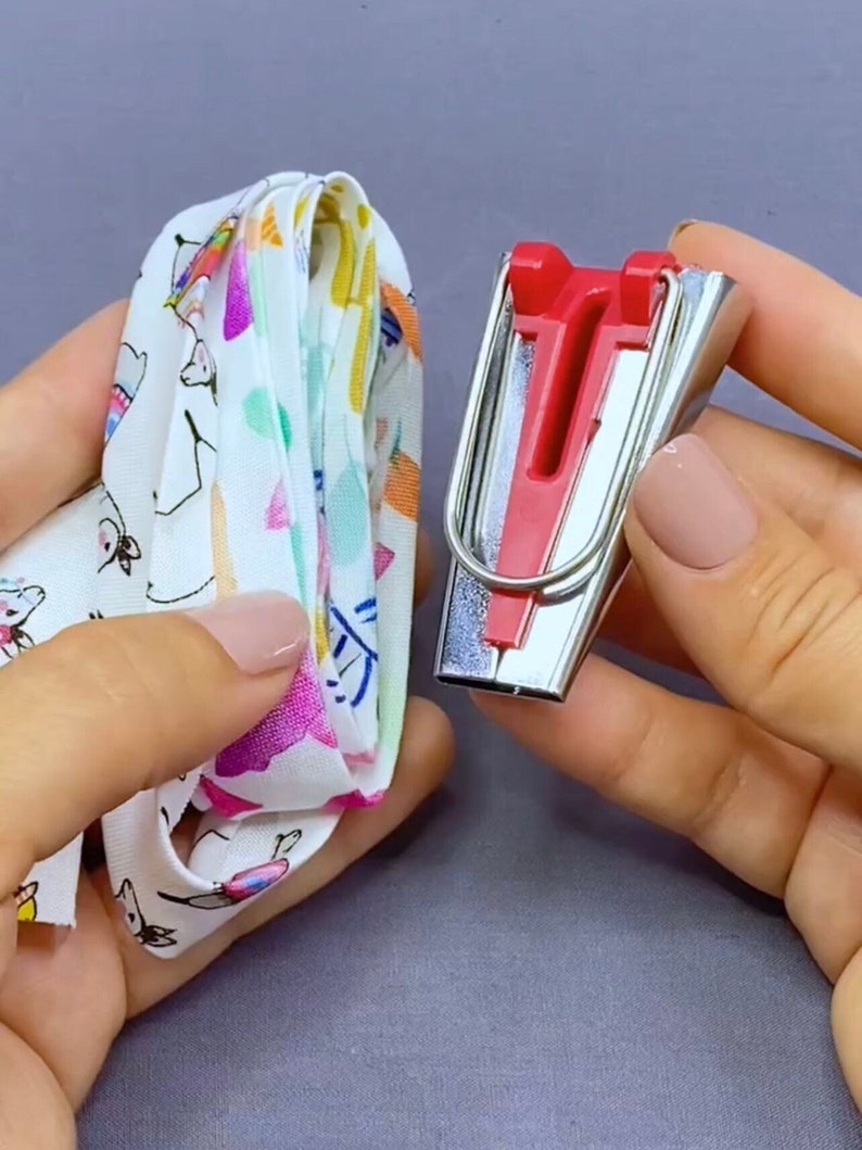 May include: A close-up of a red and silver fabric pressing tool. The tool is used to press seams in fabric. The tool is being held in a hand.