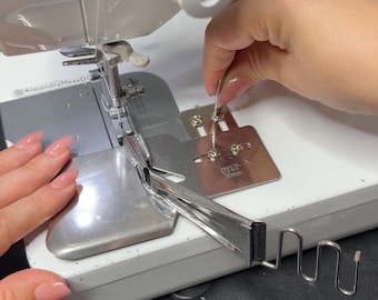 May include: A close-up of a sewing machine with a metal attachment. The machine is white with silver metal components. A hand is holding a metal tool near the attachment. The text "DYLT 30mm" is visible on the attachment.