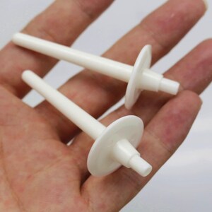 May include: Two white plastic candle holders with a round base and a long, thin stem.