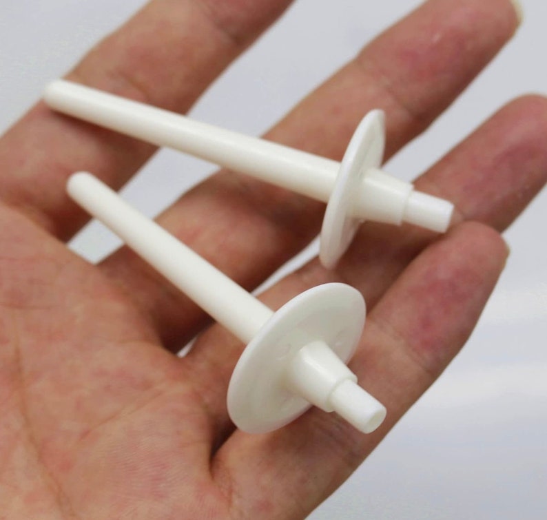 May include: Two white plastic candle holders with a round base and a long, thin stem.